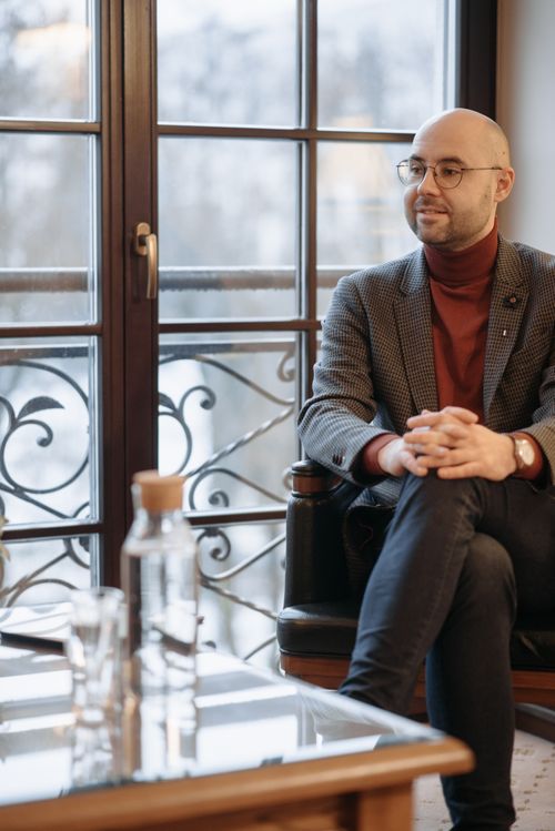 Free Balding man with eyeglasses in an elegant outfit sits in a cozy indoor setting. Stock Photo