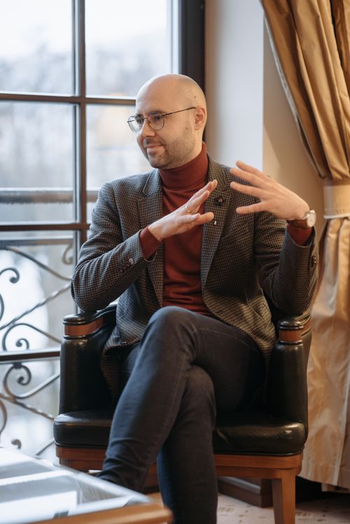 Free Well-dressed man in conversation, gesturing inside a bright office setting. Stock Photo