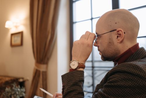 Free Side view of a bald man in glasses and suit looking thoughtfully out a window. Indoors setting. Stock Photo