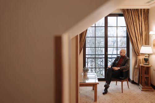 Free A man relaxes in a cozy living room with large windows and elegant decor. Stock Photo