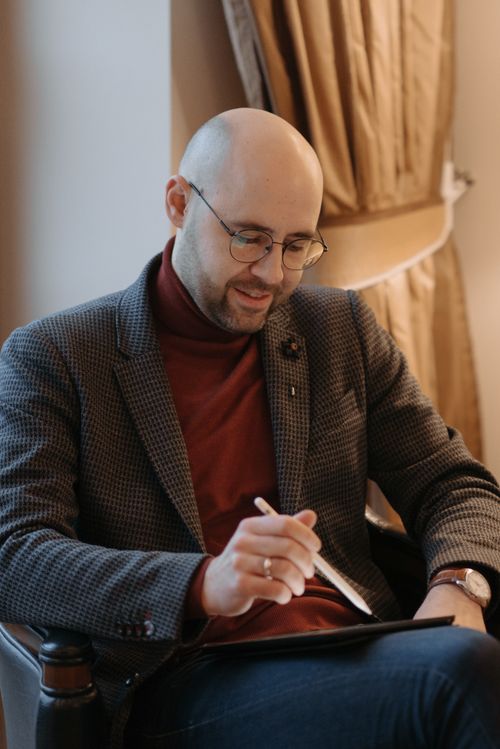 Free Bald man with glasses sitting and using a digital tablet indoors, appearing focused and engaged. Stock Photo
