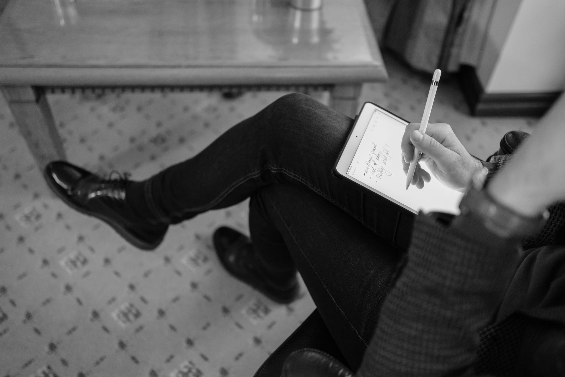 Black and white photo of a person writing on a digital tablet inside a room, showcasing modern technology.