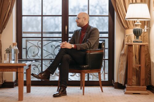 Free Man in a suit with glasses sitting by a window in a sophisticated room. Stock Photo