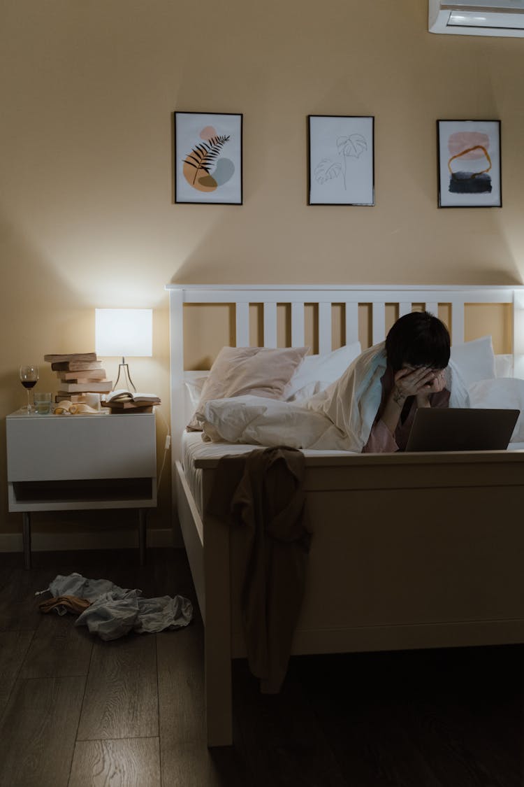 Woman Lying On The Bed With A Laptop And Hiding Her Face In Hands 