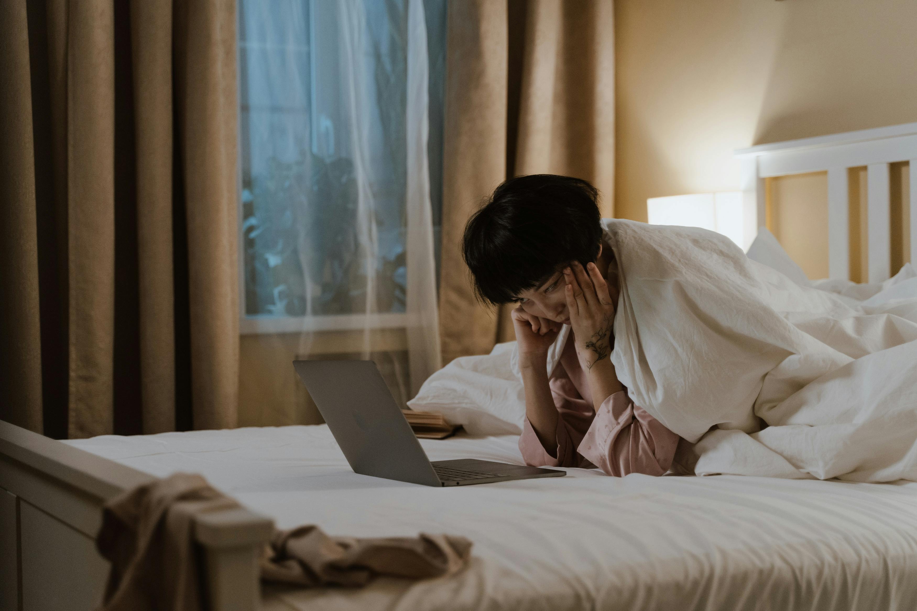 a woman lying on the bed while looking at the screen of a laptop