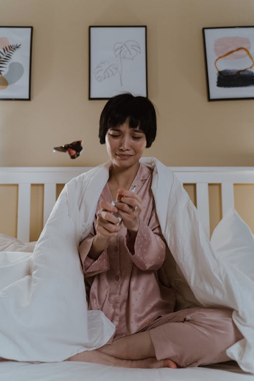 Free Crying Woman Sitting on Bed in Pajamas Stock Photo