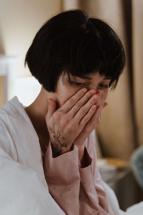 Free Portrait of a woman expressing sadness, hands covering face indoors. Stock Photo