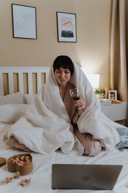 Free Woman Sitting on Bed Drinking Wine Stock Photo
