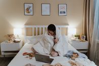 Woman in White Robe Sitting on Bed Using Silver Macbook