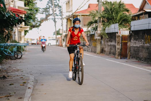 A woman in a red shirt rides a bike on a quiet urban street, enjoying a leisurely afternoon.