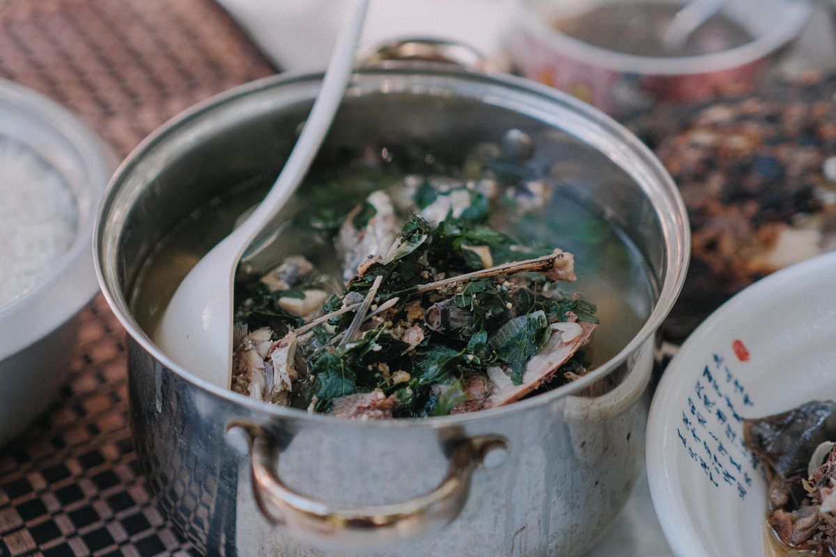 Homemade bone broth simmering in a stainless steel stockpot with fresh herbs, a traditional preparation often used for gut health