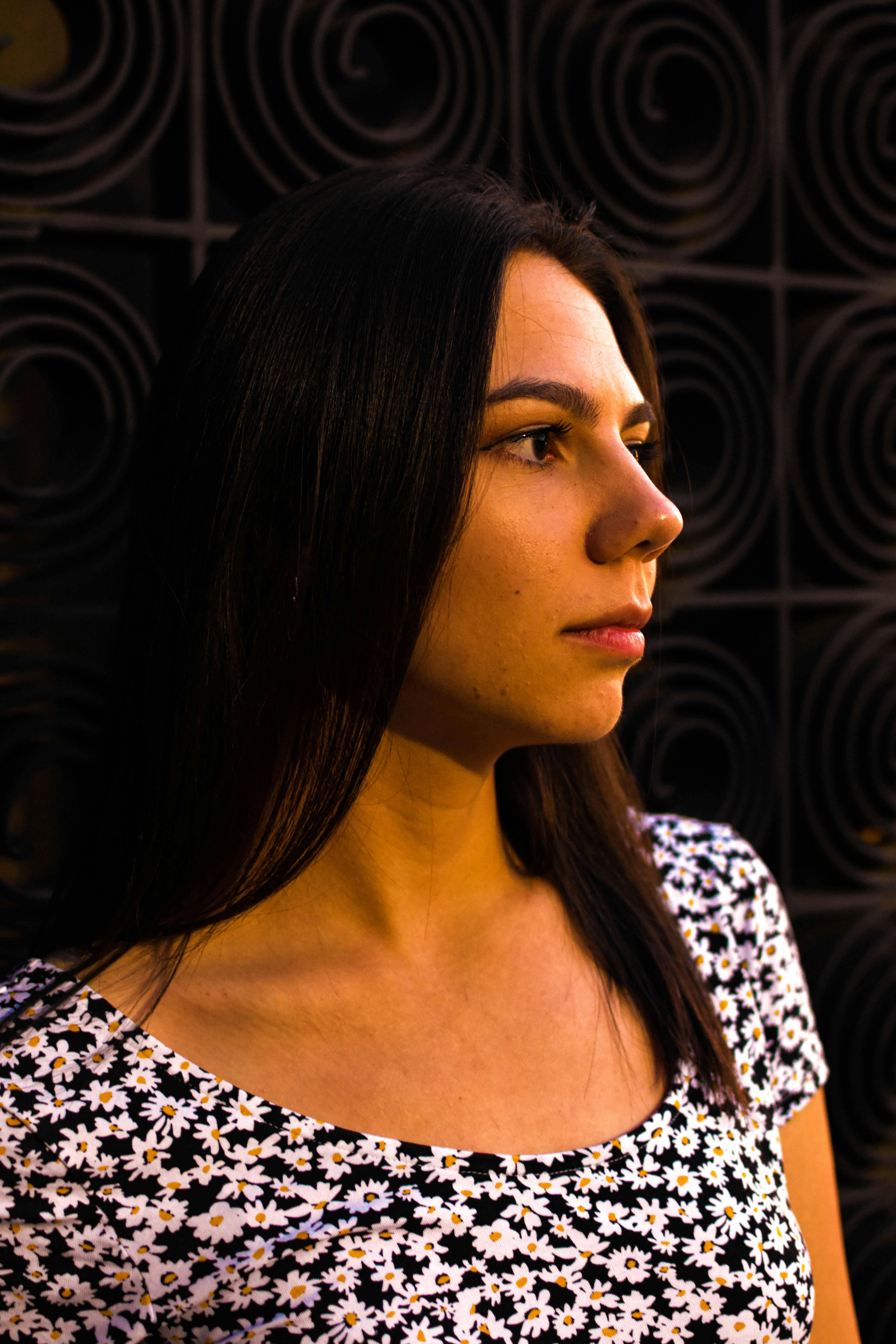 A profile portrait of a young woman wearing a floral dress against a decorative backdrop.