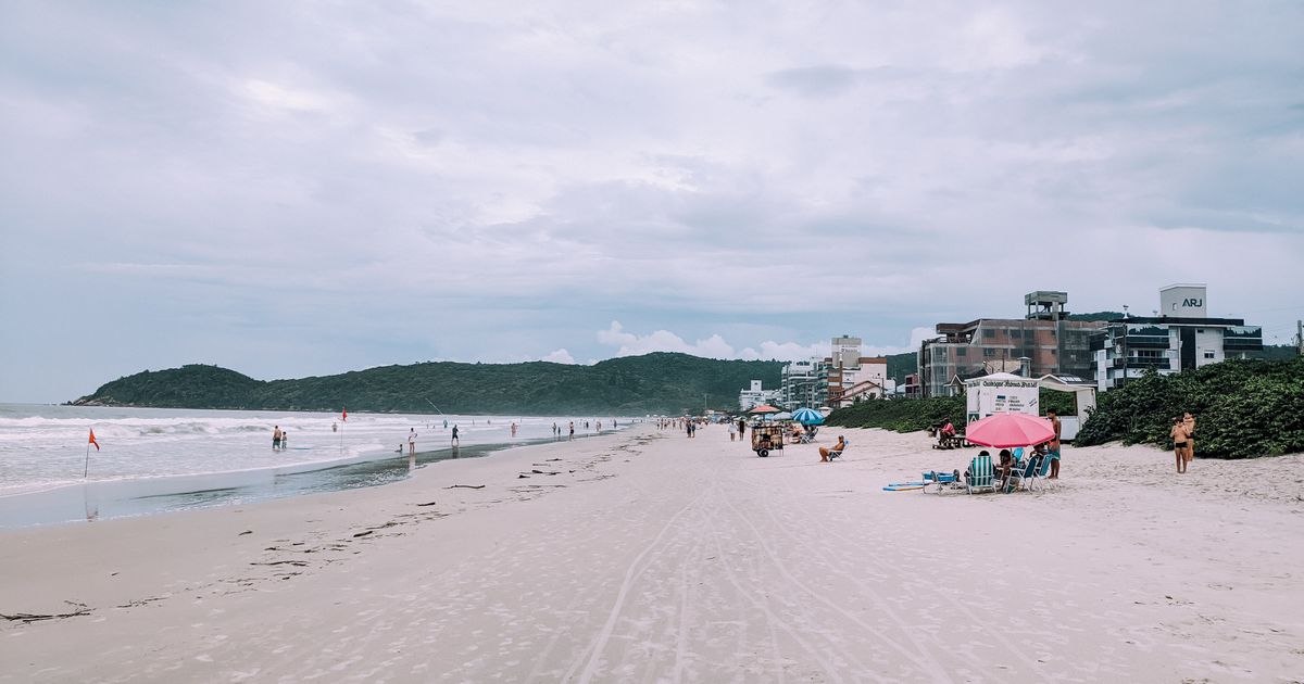 Uma cena tranquila de praia com pessoas, guarda-sóis e prédios ao longo da costa.