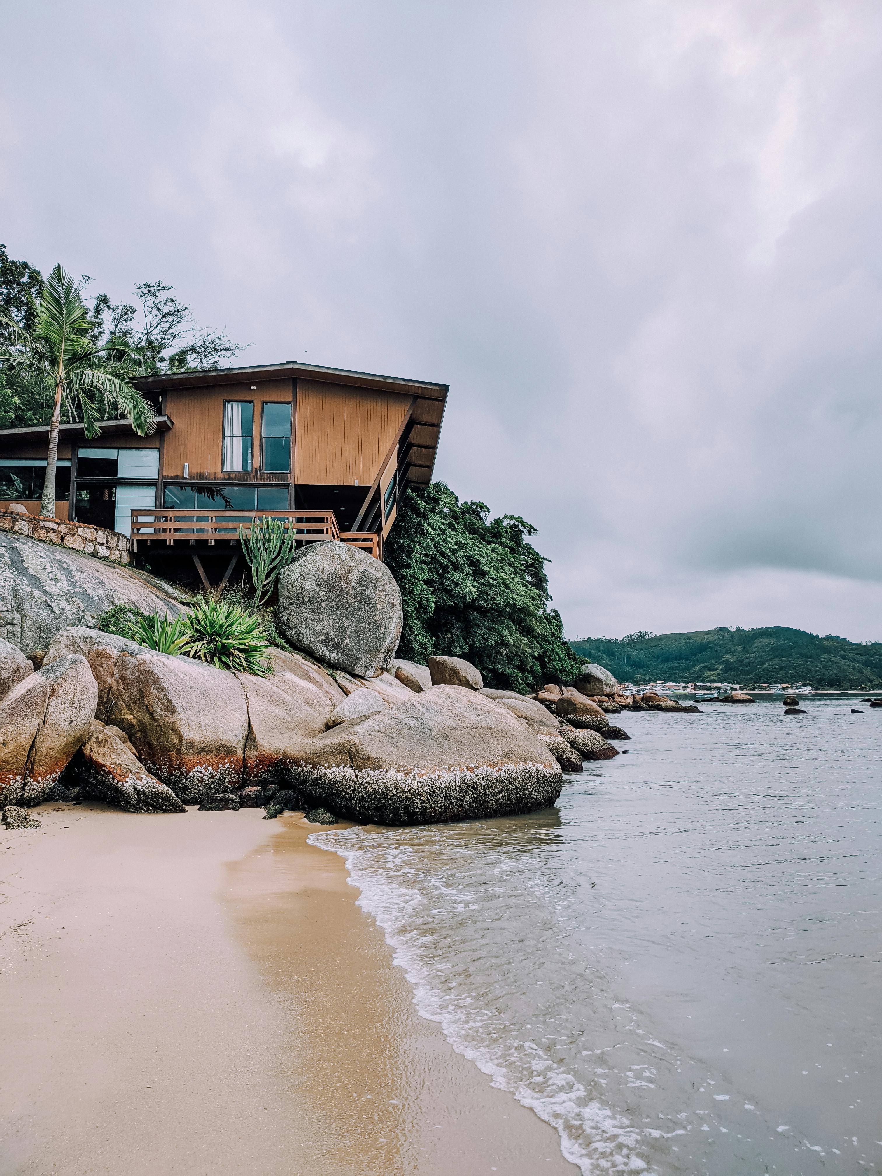 Brown Wooden House Near Body of Water and Boulders · Free Stock Photo
