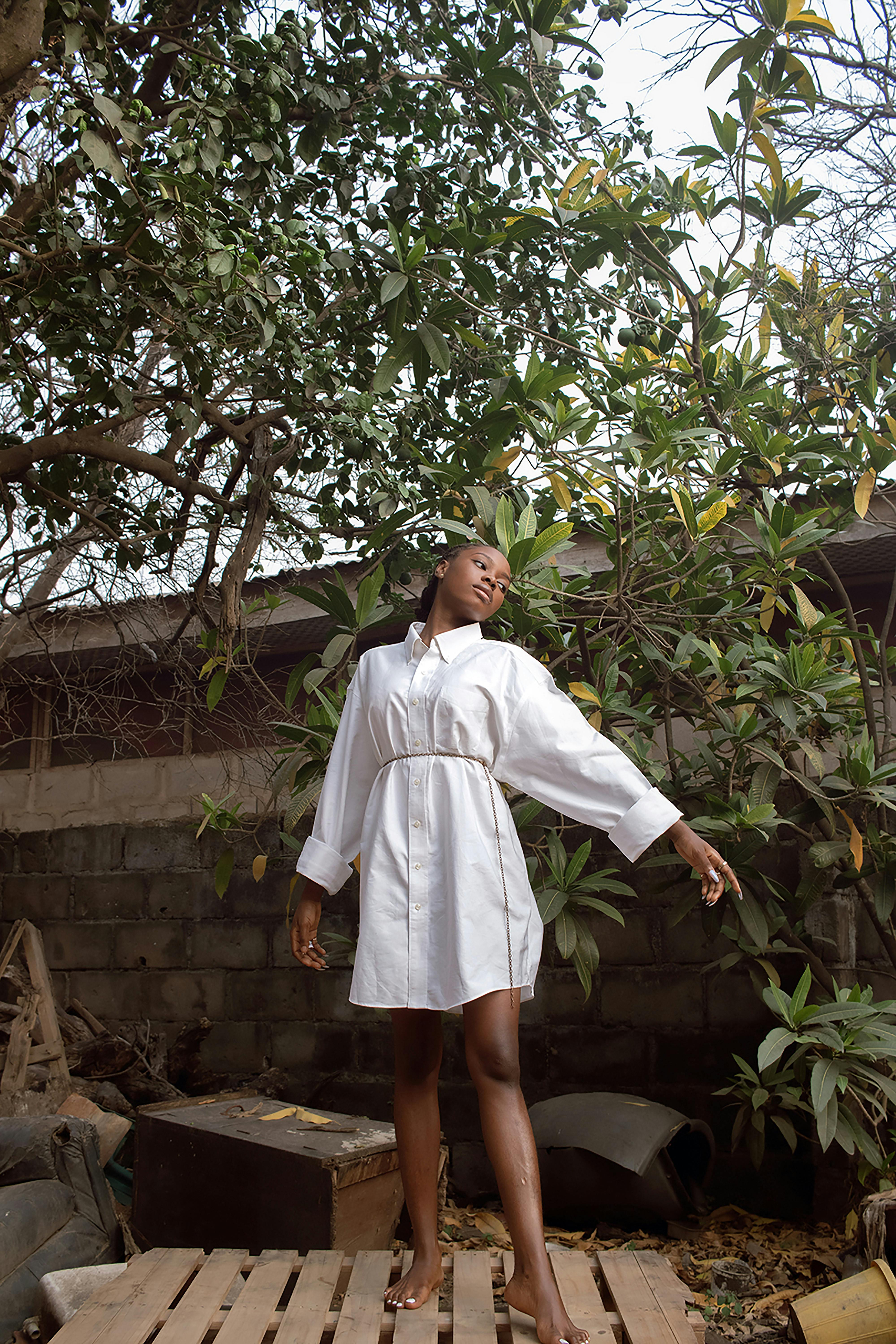 A woman poses gracefully in a backyard surrounded by lush greenery, exuding elegance.
