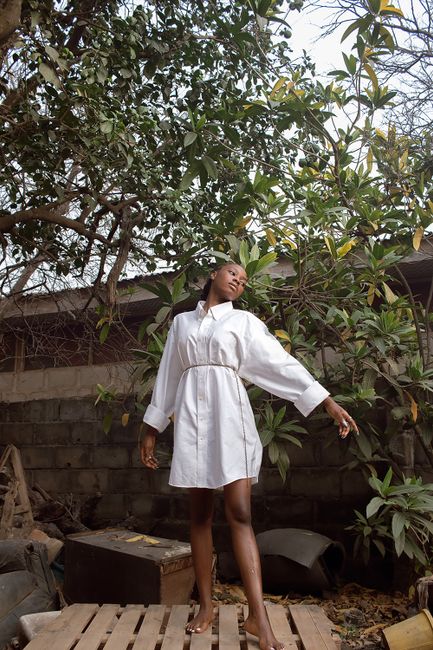A woman poses gracefully in a backyard surrounded by lush greenery, exuding elegance.