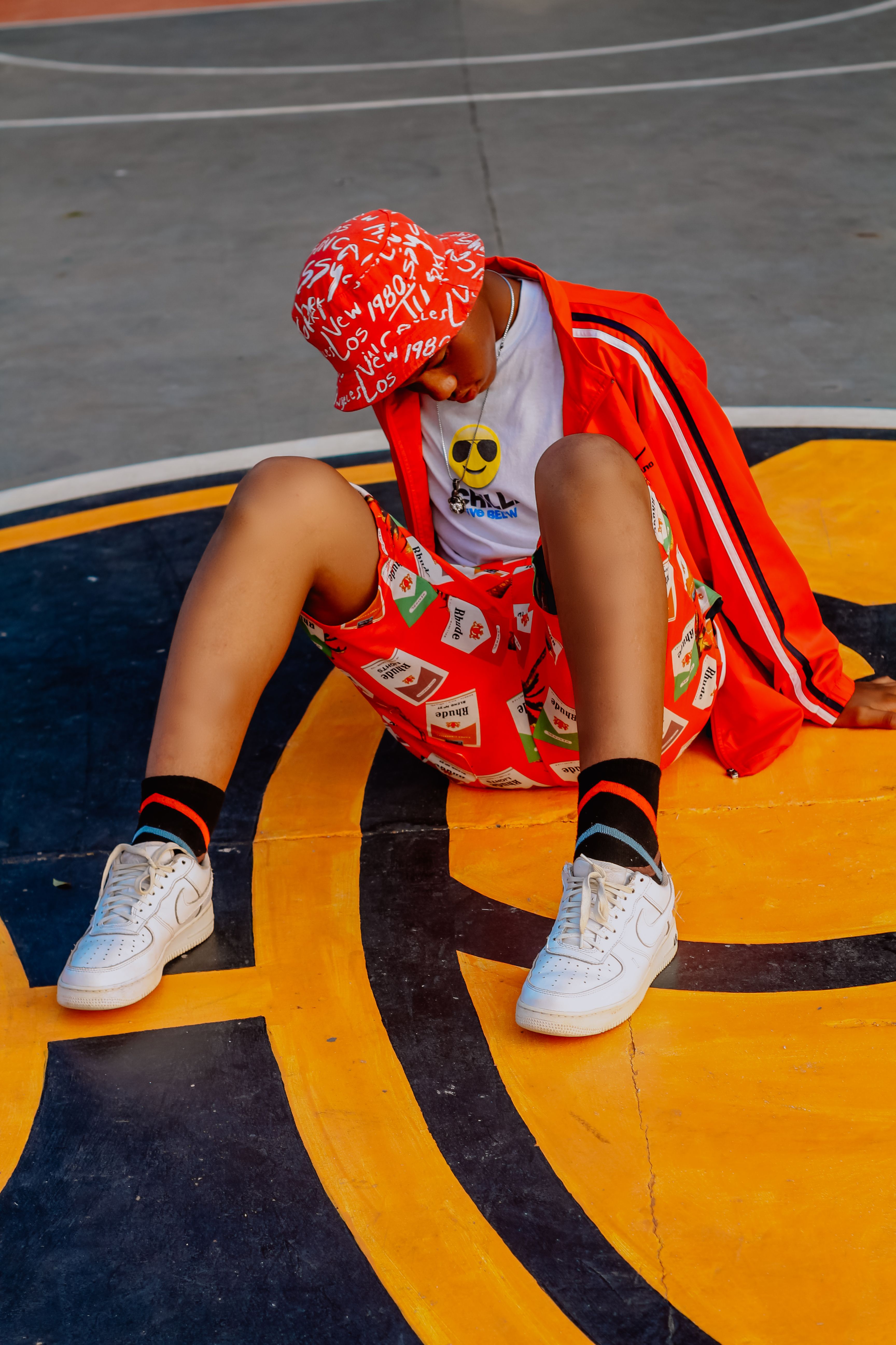 Stylish young person in colorful streetwear sitting on a basketball court.