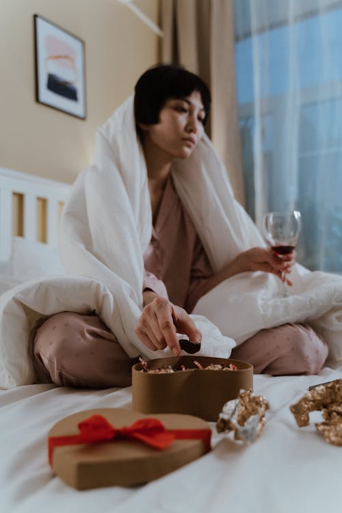 Free A Woman in Her Pajamas Eating Chocolates and Drinking Wine Stock Photo