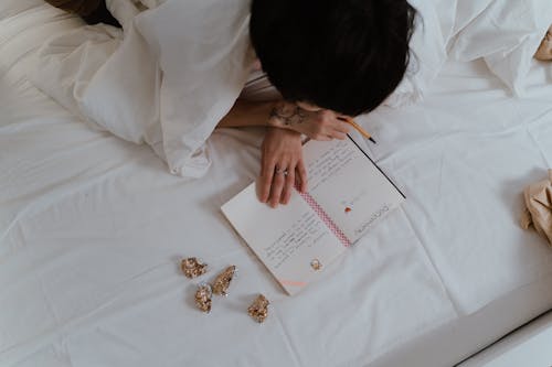 Free A Person Reading a Notebook while Lying on a Bed Stock Photo