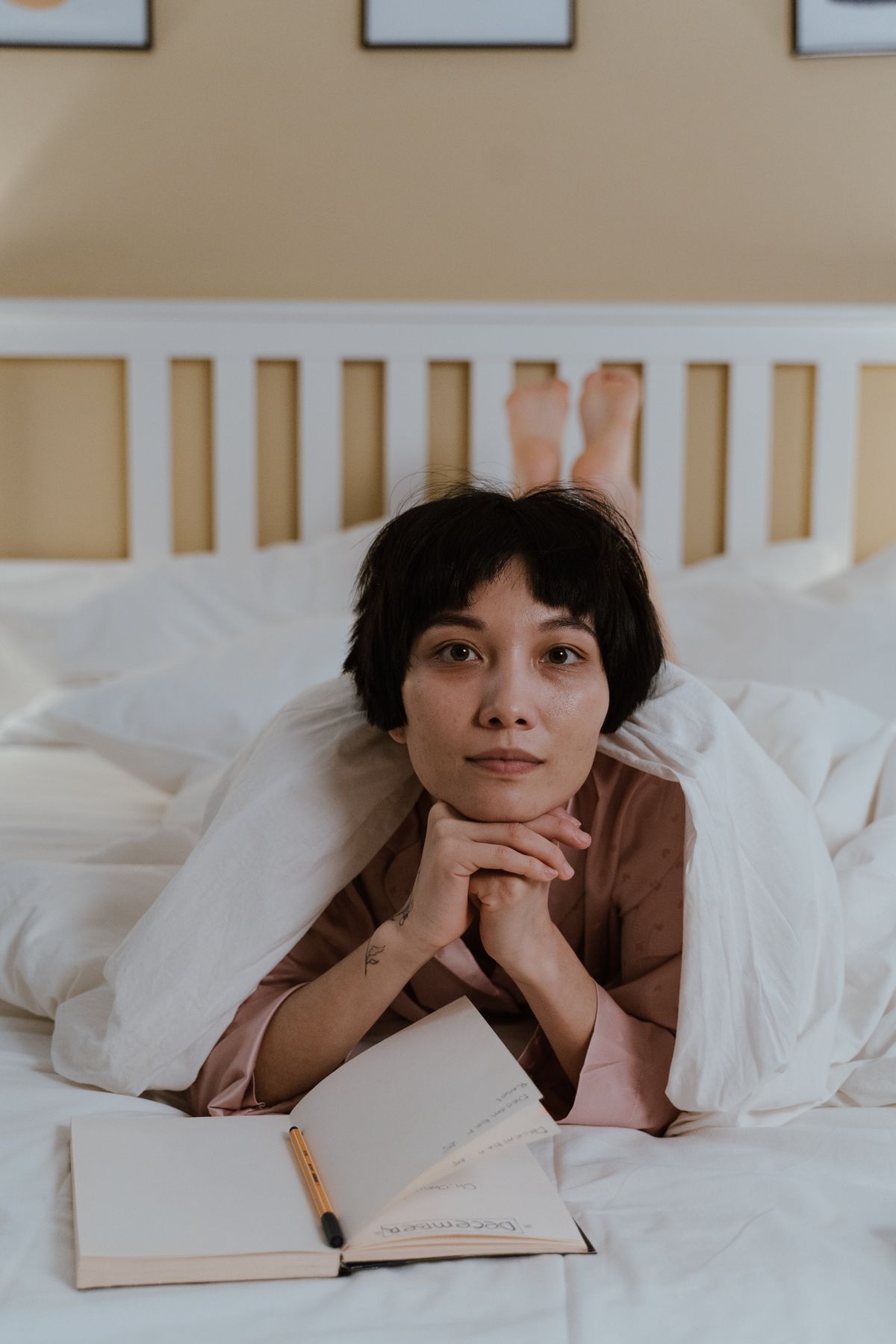 Person resting calmly in bed with a thoughtful expression, notebook nearby