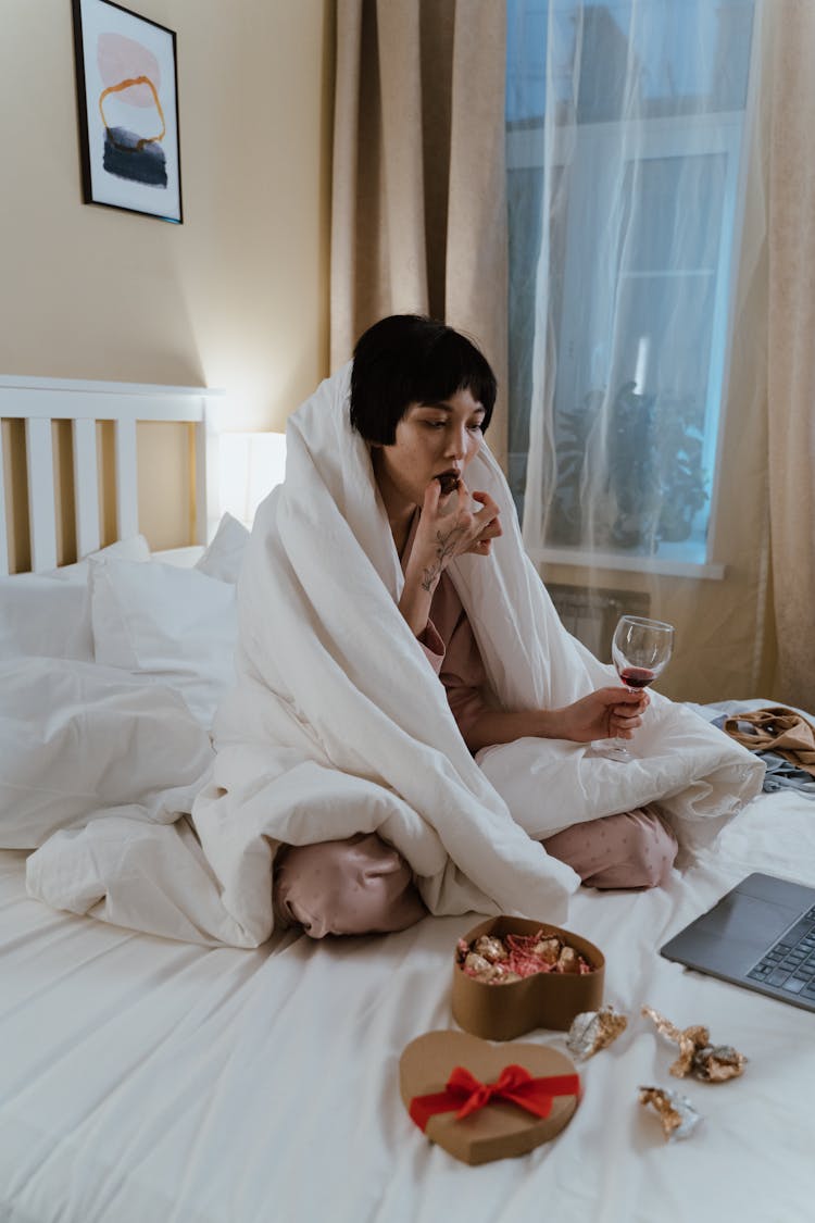 A Woman Eating While Holding A Glass Of Wine