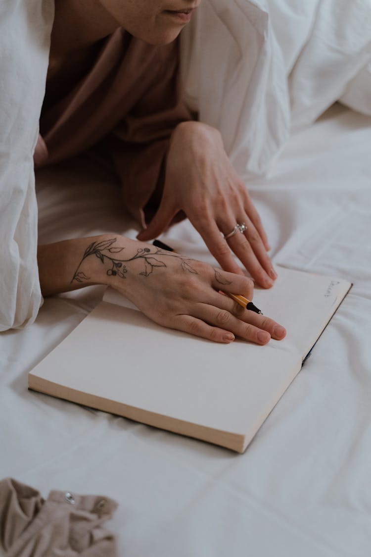 A Person Writing On A Notebook While Lying On A Bed