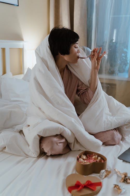 Free A Woman Drinking a Glass of Red Wine while Sitting on a Bed Stock Photo