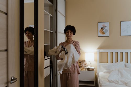 Free A Woman Standing Between a White Bed and a Closet Stock Photo