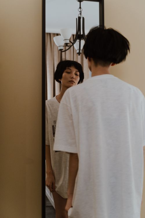 Free Woman with short hair reflecting in a mirror indoors, showcasing introspection. Stock Photo