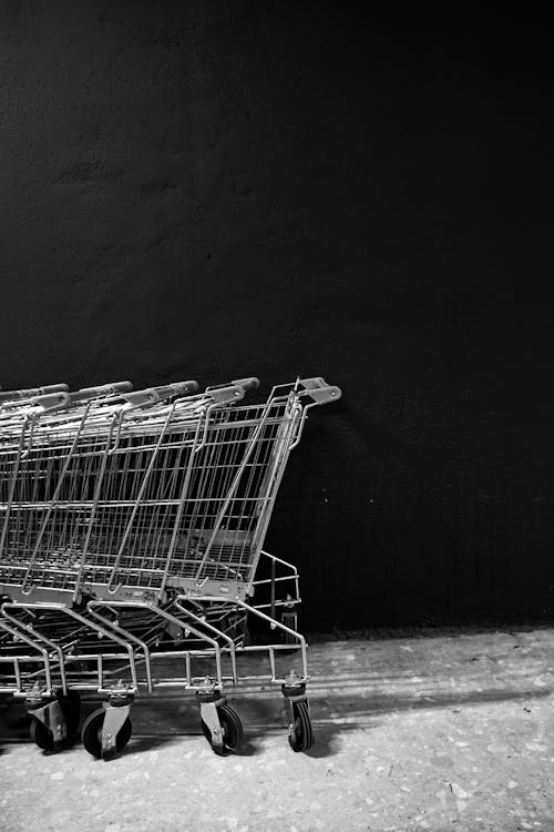 Black and white white of empty shopping trolleys standing on asphalt near black wall of supermarket