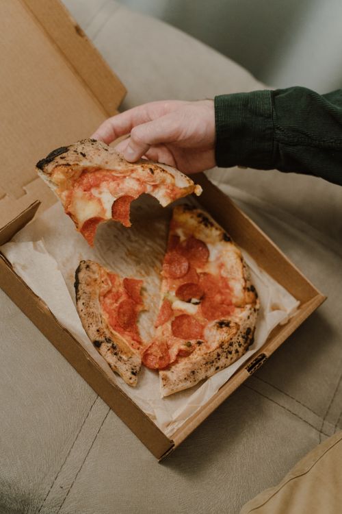 Free Close-up of a hand grabbing a slice of delicious pepperoni pizza from a box. Stock Photo