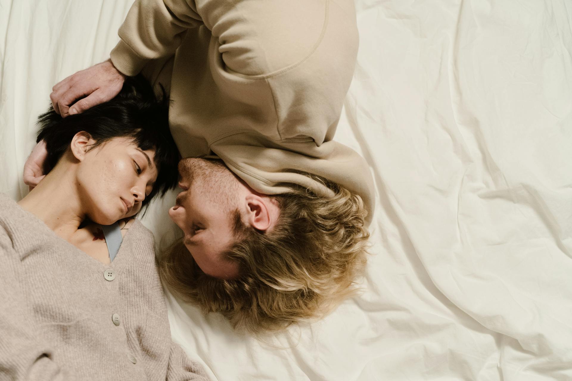 Man in Brown Hoodie Lying Upside Down on Bed Beside a Woman in Brown Sweater