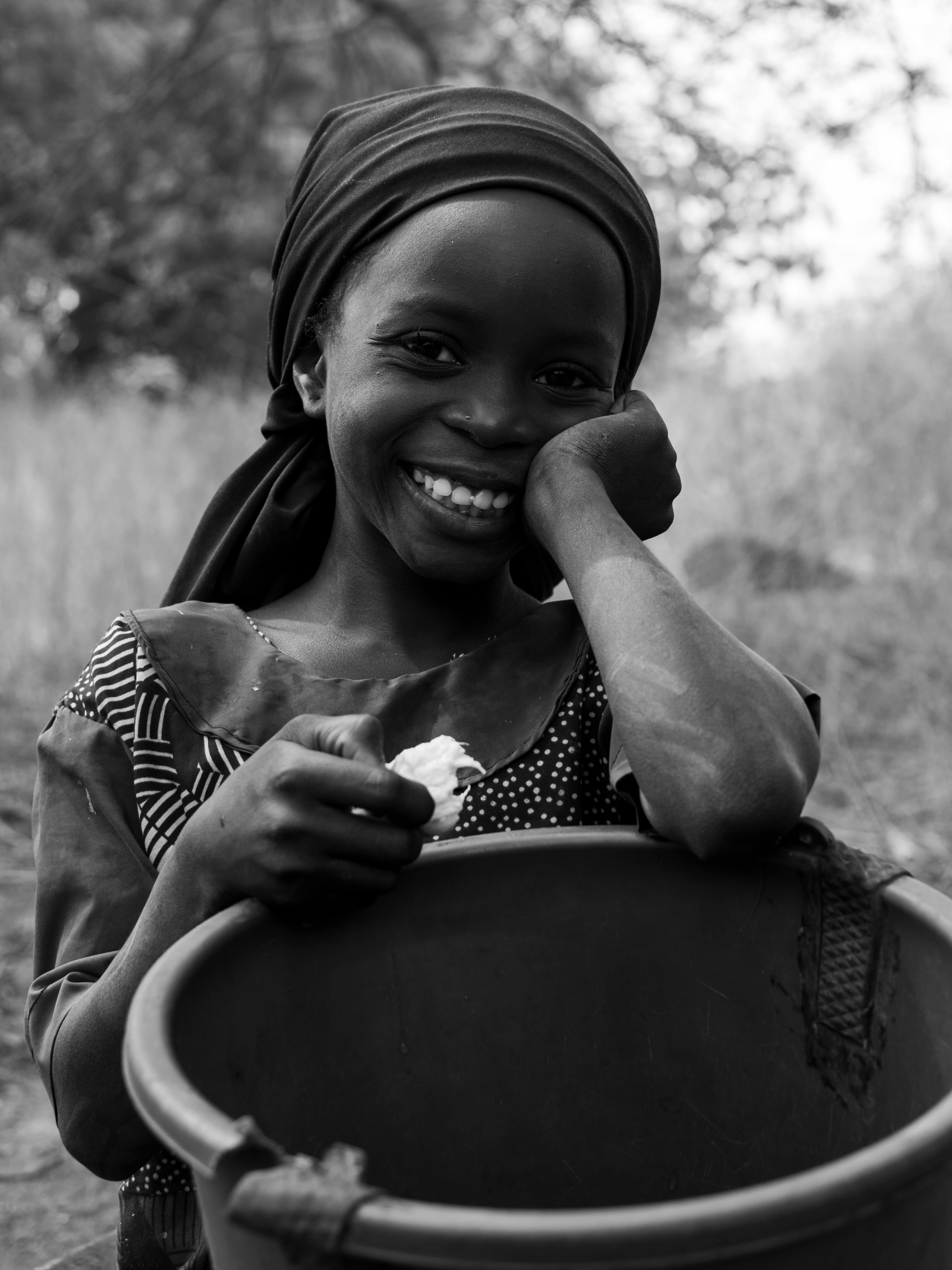 A joyful African girl with a basket, captured outdoors in black and white.