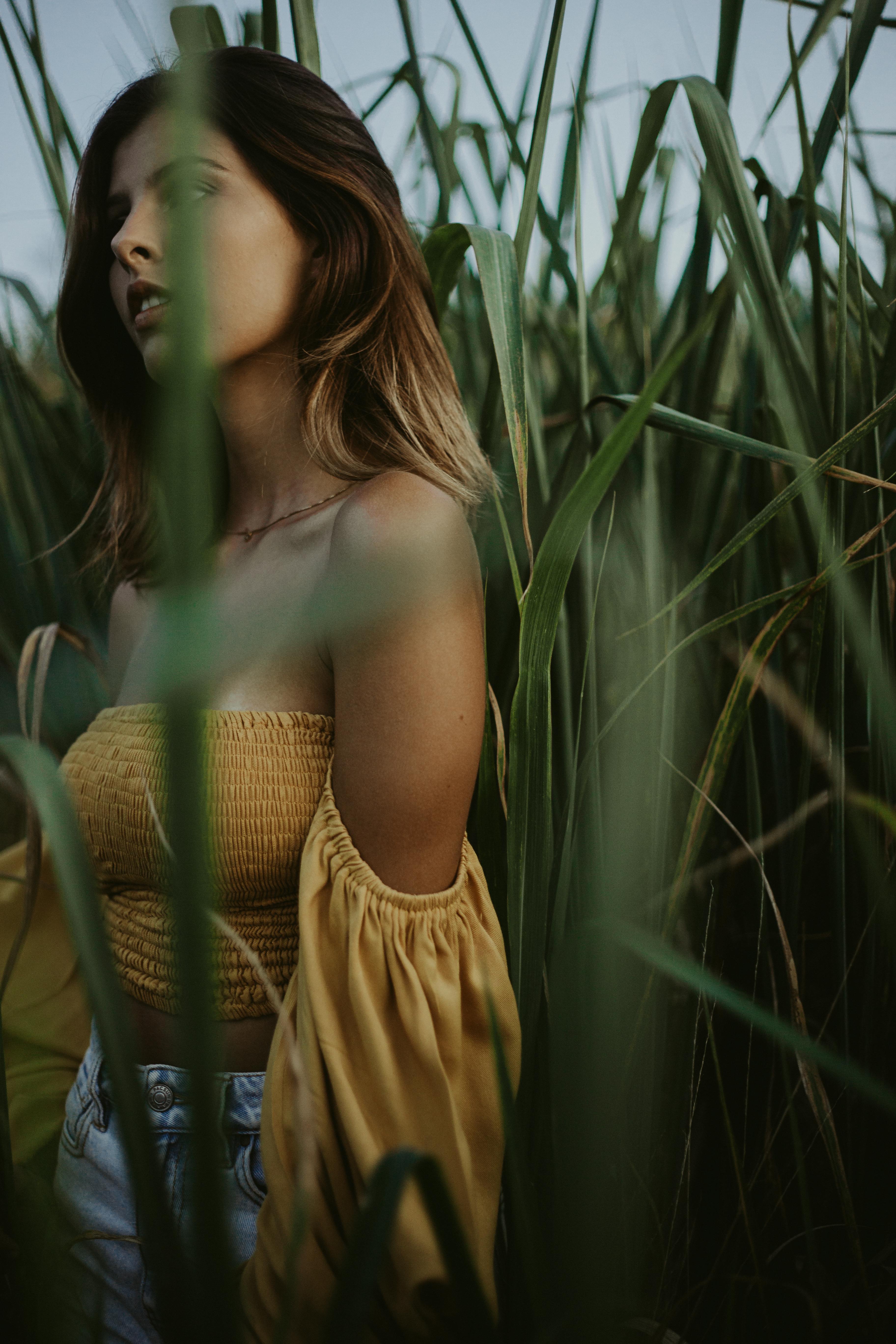 selective focus photo of a woman in a yellow off shoulder top near tall grass