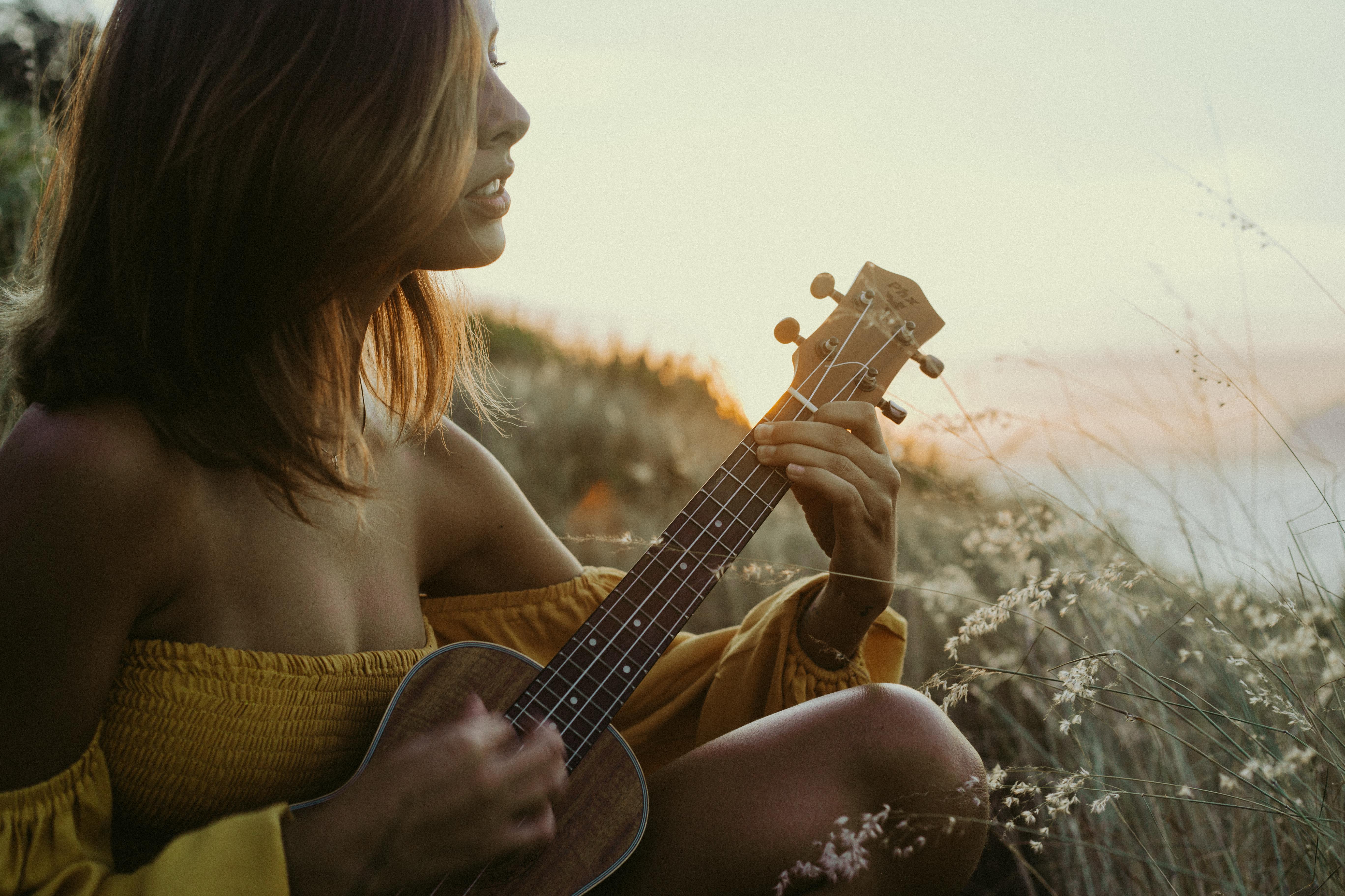 一名女子在温暖的日落草地上弹奏尤克里里琴，创造出宁静的音乐时刻