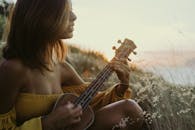 一名女子在温暖的日落草地上弹奏尤克里里琴，创造出宁静的音乐时刻