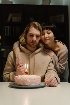 A loving couple enjoys a cozy birthday celebration with a candle-lit cake indoors.
