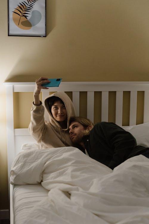 A Couple Taking a Selfie While Lying Down on a White bed · Free Stock Photo