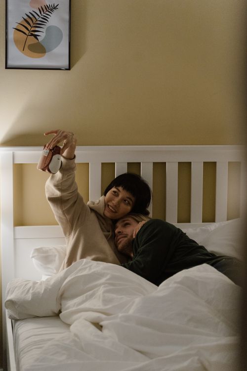 Free Happy couple taking a selfie while relaxing in bed, capturing a cozy morning moment. Stock Photo