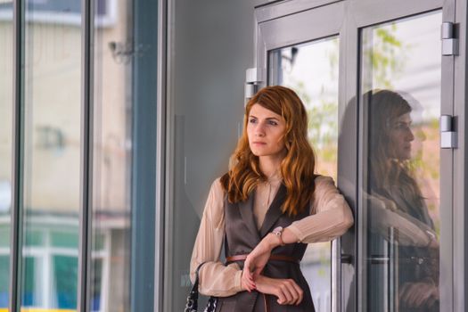 Stylish woman in urban environment standing by a glass door, reflecting thoughtful mood.