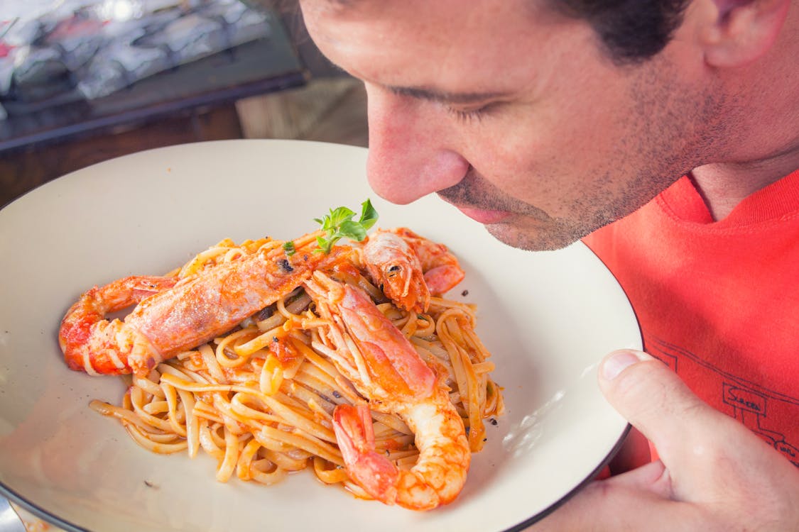 Free Man Smelling Prawn and Pasta Dish on White Ceramic Plate Stock Photo