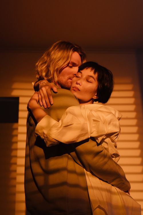Free A loving couple embraces indoors, captured in soft, warm lighting casting dramatic shadows. Stock Photo