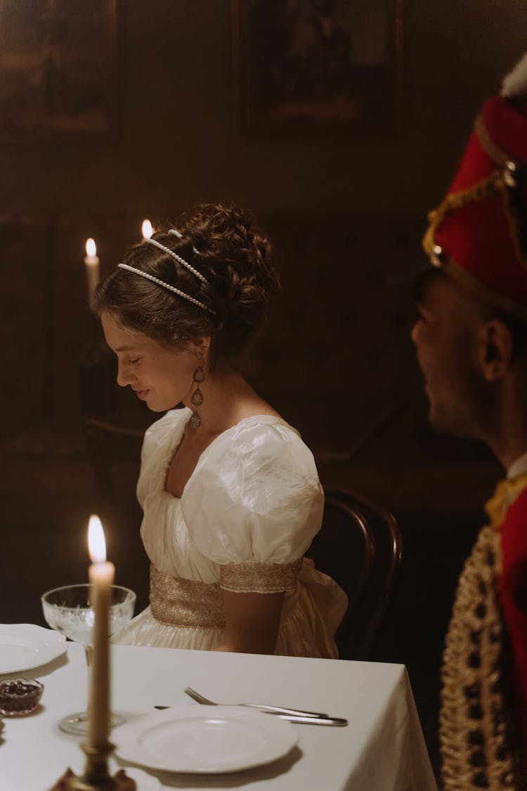 Woman In White Dress Sitting At Table With Candle 