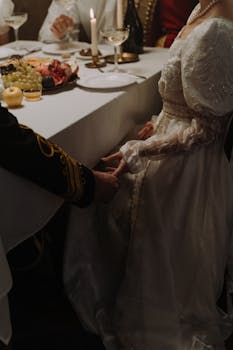 A couple in period costumes share an intimate moment during a candlelit dinner.