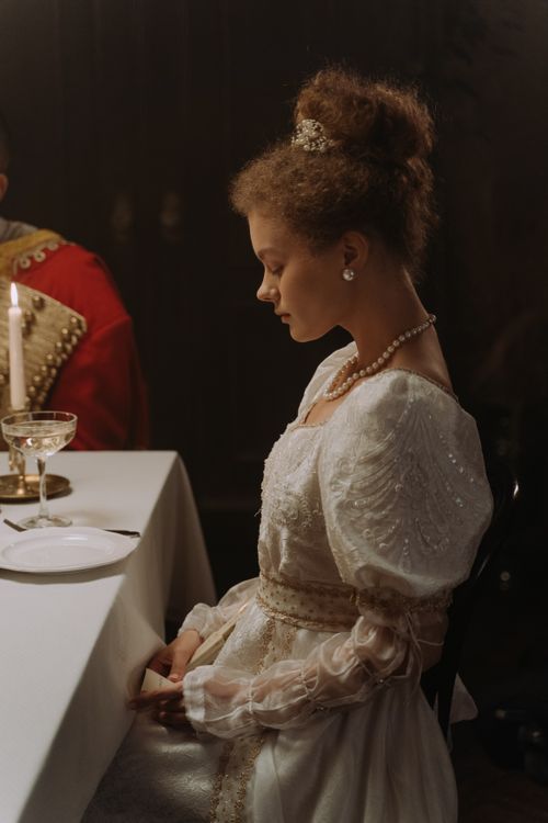 Free Portrait of a woman in 19th century attire, seated by a candlelit dinner table. Stock Photo