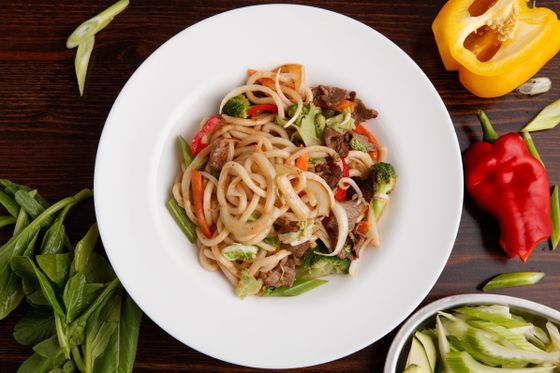 White plate of thick udon noodles tossed with beef slices, broccoli, peppers and green beans