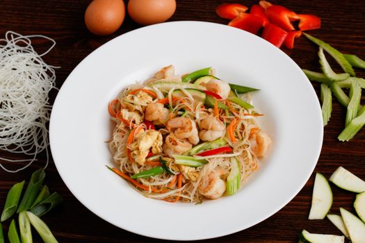 A close-up of tasty shrimp noodles with fresh vegetables on a ceramic plate.