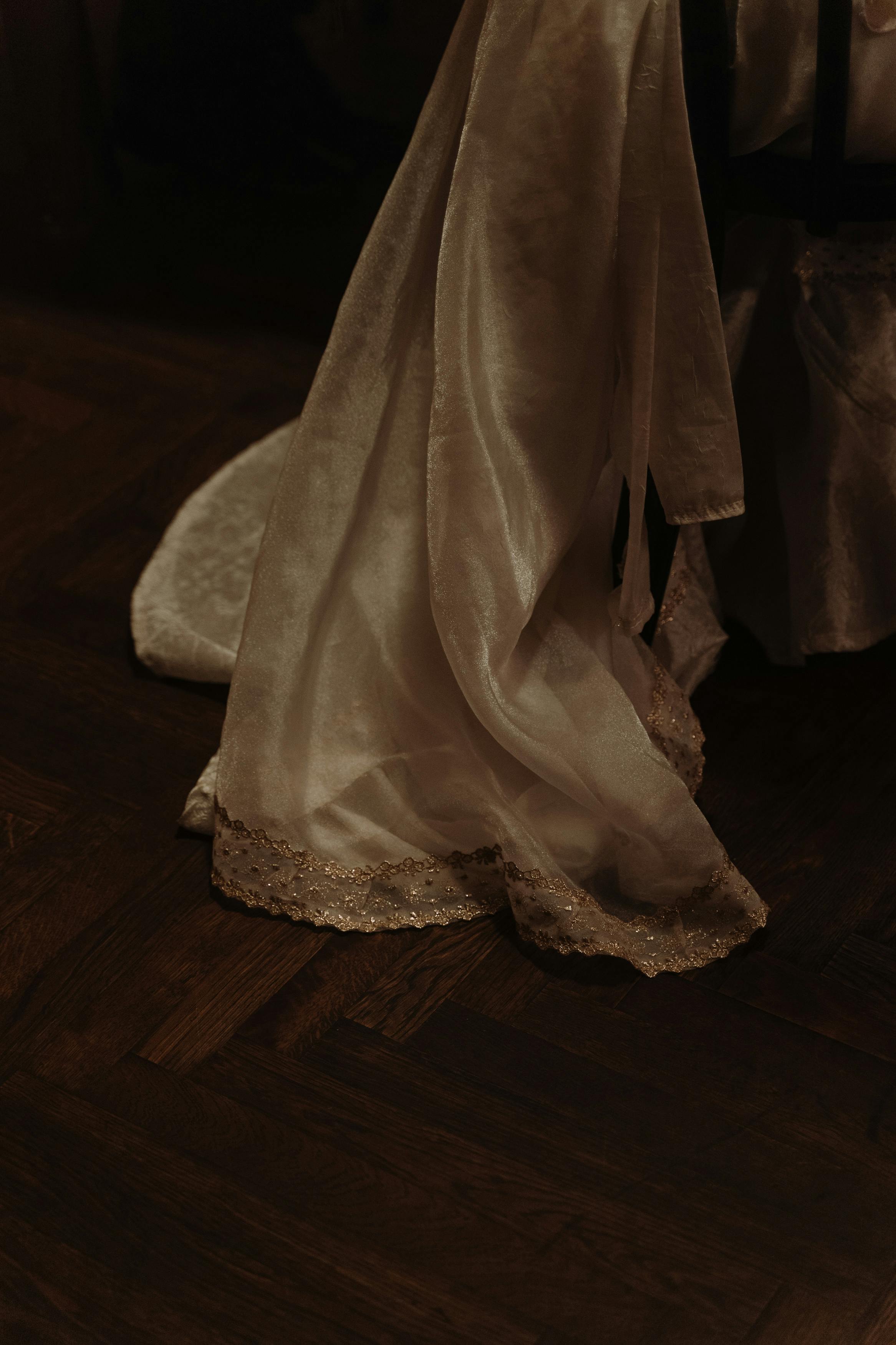 Close-up of an elegant white dress on a wooden floor, capturing its luxurious details.