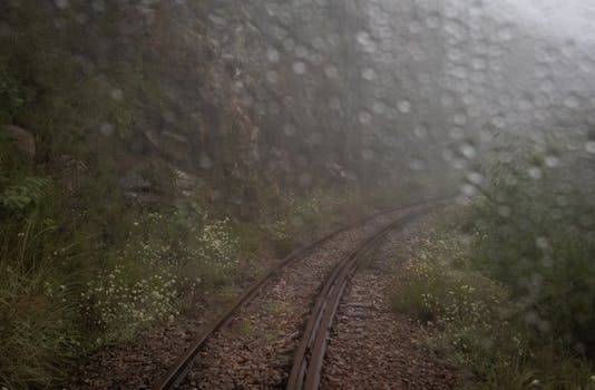 Blurred view of railway tracks through rain-soaked window in a misty countryside setting.