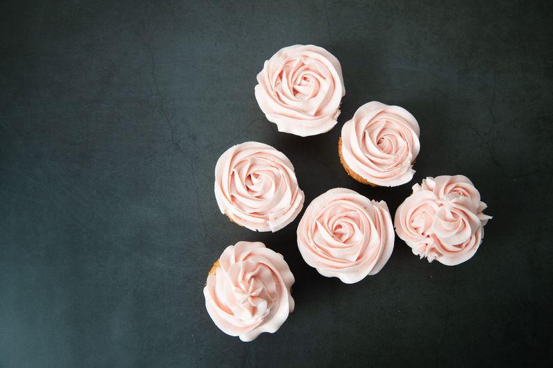Six cupcakes with pale pink frosting on a dark surface